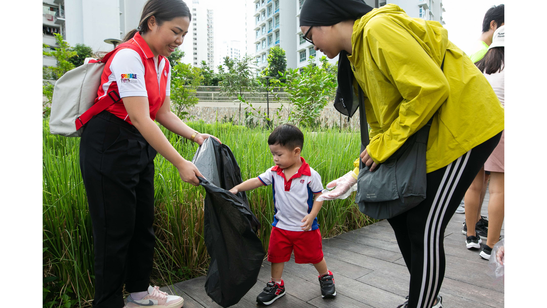 Omar and his mother throwing litter into a plastic bag held by teacher Ms Corum